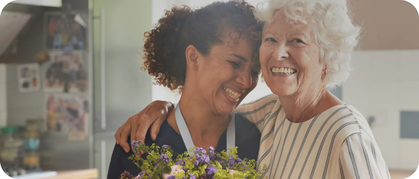"Twee vrouwen glimlachen naar elkaar, wat het belang van compassievolle zorg voor de gezondheid van de peristomale huid weerspiegelt."