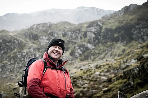 una persona sonriendo con montañas en el fondo
